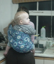 A mum carries her baby on her back in a pouch while doing chores