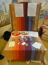 A Girasol wrap serves as a tablecloth for the Sheffield Babywearers stand, with cake and flyers on it.