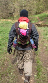 Intrepid dad carries an older baby on his back in a Boba (soft structured carrier) while on a walk in the country
