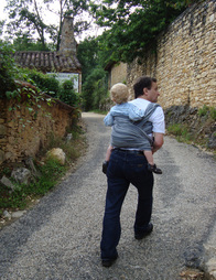 A man walks up a country lane with his toddler son wrapped on his back