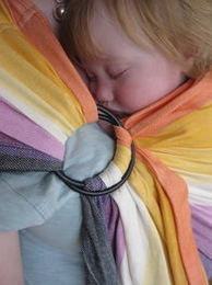 A baby snuggles to sleep on his mum's front in a colourful stripey ring sling