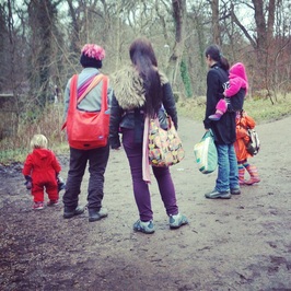 Three babywearing mums with their kids having a walk in the woods.