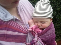 A sleeping newborn snuggles into its mum in a ring sling